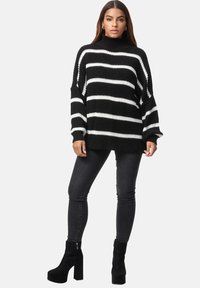 Gestreifter Strickpullover in Schwarz-Weiß mit hohem Ausschnitt, weiten Ärmeln und gerippten Bündchen, kombiniert mit dunklen Skinny-Jeans und Plattform-Stiefeln.