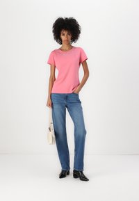 Rosa Kurzarm-T-Shirt mit Strassverzierung am Ausschnitt, kombiniert mit hellblauen geraden Jeans und schwarzen Stiefeletten mit Absatz.