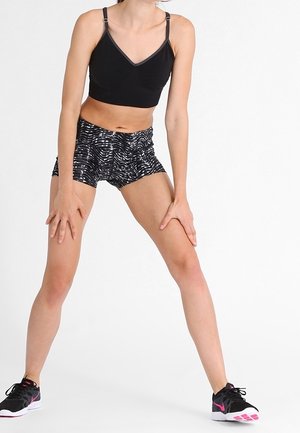 Černá sportovní podprsenka s nastavitelnými ramínky, spárovaná s šortkami s černobílým vzorem. Černé sportovní boty s růžovými detaily.