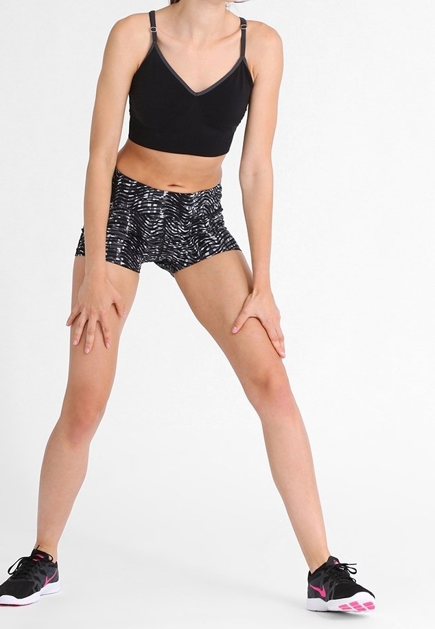 Czarny stanik sportowy z regulowanymi ramiączkami, zestawiony z szortami w czarno-białe wzory. Czarne buty sportowe z różowymi akcentami.