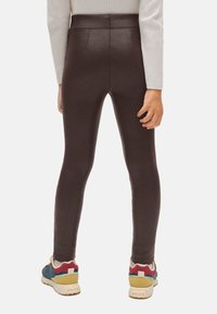 Leggings de imitación de cuero marrón con una cinturilla alta y sin costuras visibles. Combinados con zapatillas coloridas con acentos texturizados.