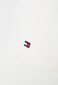 Casquette de baseball en coton blanc avec un petit logo brodé en bleu marine, rouge et blanc sur le devant. Design classique avec visière incurvée.