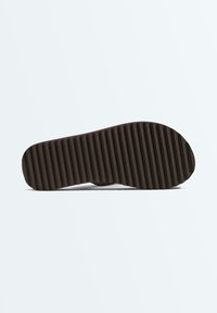 Sandal sole viewed from below showing dark brown ribbed tread pattern.