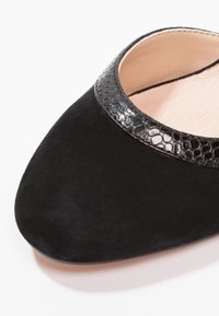 Černé semišové boty s lesklým černým hadím vzorem na límci. Zaoblený design špičky a hladké vnitřní podšívání.