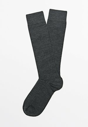 Calzini alti al ginocchio di colore grigio scuro, distesi su sfondo bianco, con un calzino leggermente sovrapposto all'altro.