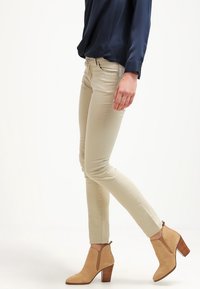 Beiga slim-fit byxor gjorda av en bomullsblandning med en slät yta. Kombinerat med bruna ankelstövlar och en mörkblå blus.