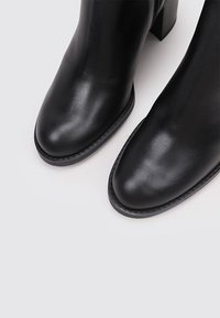 Botas de cuero negro hasta el tobillo con punta redonda, tacón cuadrado, textura suave y costuras sutiles a lo largo de la suela.