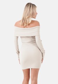Off-Shoulder-Rippstrickkleid in Hellbeige, mit langen Ärmeln und einer figurbetonten Silhouette, die über das Knie reicht.