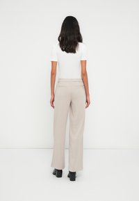 Light beige wide-leg trousers with a textured finish, featuring an elastic waistband and two back pockets, paired with black heeled shoes.