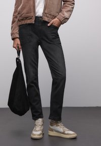 Jeans neri con cuciture a contrasto, tasche frontali e design a gamba dritta. Abbinate a sneakers beige e bianche e a una borsa tote nera.