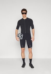 Vêtement de cyclisme noir avec un haut zippé et un short ajusté. Comprend un casque gris et des lunettes de soleil noires, mettant en avant un design élégant et moderne.