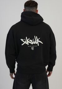 Črna kapuca z velikim belim grafičnim besedilom na hrbtni strani, ki vsebuje ime blagovne znamke "Siksilk" in frazo "Ride or Die."