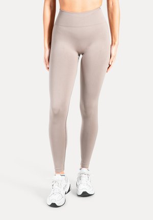 Beige leggings med høj talje, glat tekstur og tætsiddende design, kombineret med hvide atletiksko med sorte og grå detaljer.