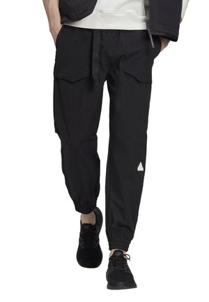 Persoon met zwarte cargobroek met elastische boorden en zwarte sneakers, lopend met handen in de zakken.