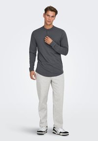 Donkergrijze henley met lange mouwen en drie knopen bij de kraag, gecombineerd met lichtgrijze sweatpants en zwart-witte sneakers.