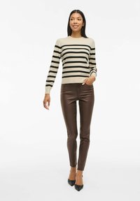 Pull rayé beige avec des rayures noires, associé à un pantalon skinny marron et des escarpins noirs à bout pointu. Texture lisse, coupe décontractée.