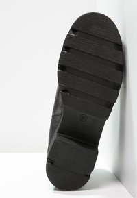 Suela de zapato negra con un patrón estriado, fabricada de goma texturizada con un diseño robusto. Talla marcada como 37 en la superficie.