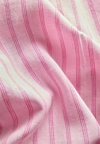 Mykt rosa stoff med tynne, vertikale magenta striper og synlig vevd tekstur, vist i myke folder.