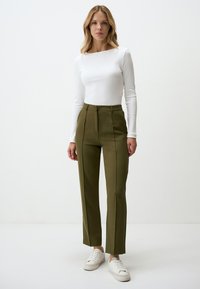 White long-sleeve top paired with olive green tailored pants featuring a high waist, front seams, and side pockets. White sneakers complete the look.