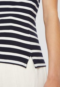 Marineblauw en witte gestreepte tanktop van textuurstof, met een zijsplitdetail, gecombineerd met witte broek.