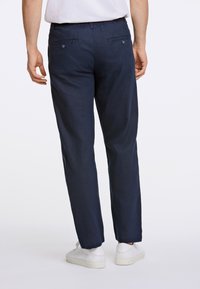 Tmavě modré kalhoty s volným střihem, zadními kapsami a knoflíkovým zapínáním, vyrobené z lehkého materiálu. Spárovány s bílými teniskami.