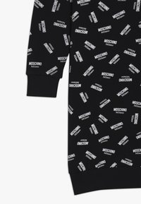 Černý oděv s bílým potiskem "Moschino Milano" po celém povrchu. Vybavený žebrovanými manžetami a měkkou texturou. Design zahrnuje různé orientace písma.