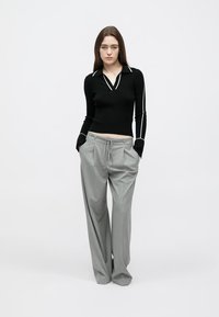 Black ribbed sweater with a V-neck and white piping, paired with loose, light gray trousers with a drawstring waist. Plain background.