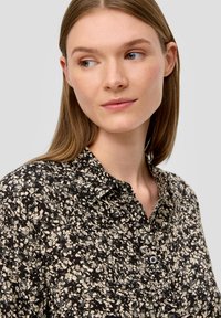 Zwart en crèmekleurig gestreept shirt met een kraag, voorzien van een gestructureerde stof en knoopsluiting aan de voorkant, gedragen door een model.