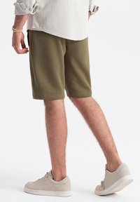Shorts en coton vert olive à coupe décontractée, avec poches latérales et texture lisse. Assortis à des baskets beige clair.