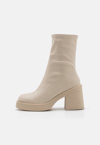 Beige knielange Stiefel mit Absatz aus glattem Leder. Sie haben einen klobigen quadratischen Absatz und eine Plateausohle für zusätzliche Höhe.
