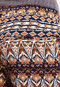 Mönstrade leggings i flera färger med en marinblå bakgrund och geometriska mönster i orange, brunt och krämvitt, samt en diskret sidoficka.