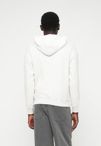 Casaco de capuz cinza claro com cordão, bainha e punhos canelados, mostrado de costas, combinado com jeans denim cinza.