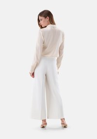 Cream satin blouse with a collar, paired with white wide-leg trousers. The outfit features tailored seams and soft texture.
