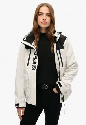 White waterproof jacket with black accents, featuring zippers, a high collar, and the word "SUPER" printed on the front. Textured inner layer visible.