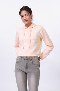Sweatshirt à capuche court en pêche clair avec un motif chevron texturé. Associé à un jean gris taille haute, affichant un design élégant.