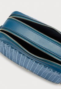 Μπλε τσάντα με φερμουάρ, με υφή στο κάτω μέρος και λείο άνω μέρος. Διακριτικά ασημένια μεταλλικά στοιχεία είναι ορατά.