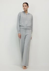 Grauer Hoodie und passende Jogginghose aus weichem Stoff. Der Hoodie hat eine Fronttasche und einen Reißverschluss; die Hose hat einen lässigen Schnitt.