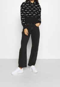 Svart hoodie med vita abstrakta mönster, ribbade mudd och fåll. Tillsammans med högmidjade svarta vida jeans och vita platform sneakers.