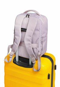 Fioletowy plecak z tkaniny, z regulowanymi szelkami, stoi na teksturowanej żółtej walizce twardej z czarnym uchwytem i zamkiem błyskawicznym.