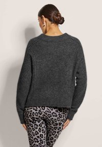 Donkergrijze wollen trui met een ronde hals en lange mouwen, met een losse pasvorm en een geribde zoom, gecombineerd met legging met luipaardprint.