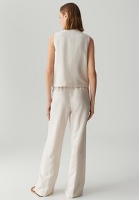 Mouwloos beige topje gecombineerd met losse beige broek. Beide zijn gemaakt van textiel met een ontspannen, minimalistisch ontwerp.