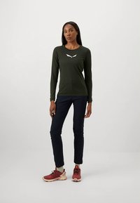 Tumesinine pükstega ja punaste spordijalanõudega kombineeritud tumeroheline pika varrukaga särk, millel on lihtne valge logo rinnal.