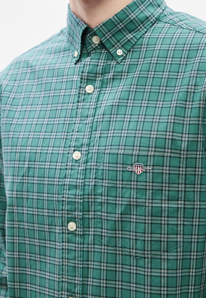 Green plaid button-up shirt made of cotton, featuring white buttons, an embroidered logo on the left chest, and a pocket.