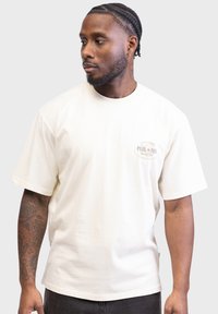 T-shirt en coton couleur crème à manches courtes, avec un petit logo imprimé sur la poitrine et une coupe décontractée. Design minimaliste.