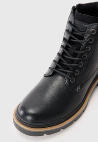 Botte en cuir noir avec finition texturée, bout rond, design à lacets, œillets en métal et semelle en caoutchouc tan contrastante pour une meilleure adhérence.