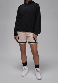 Sudadera negra con capucha y bolsillo frontal; pantalones cortos rosa claro con borde negro; zapatillas blancas de caña alta; calcetines negros hasta el tobillo.