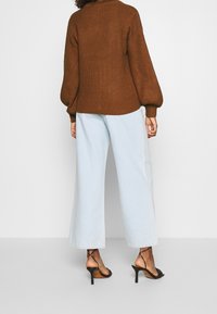 Brun stickad tröja med hög krage, uppblåsta ärmar, kombinerad med ljusblå vida jeans och svarta remsandaler.