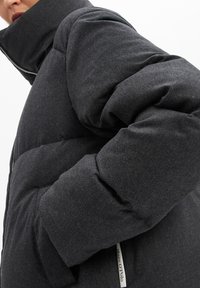 Schwarze Pufferjacke mit hohem Kragen, gestepptem Design, Reißverschluss und seitlichen Taschen. Aus weichem, mattem Stoff gefertigt.