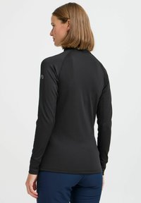 Zwart sportshirt met lange mouwen en hoge kraag, gemaakt van een gladde stof. Heeft raglanmouwen en minimale branding op de schouder.