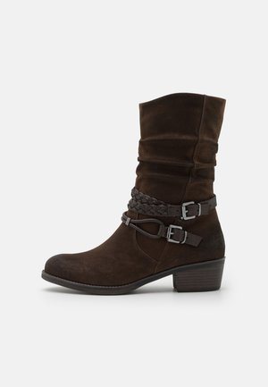 Bottines en suede marron avec un design plié, accent de ceinture tressée et boucles en argent. Présentent un bout rond et un talon empilé.